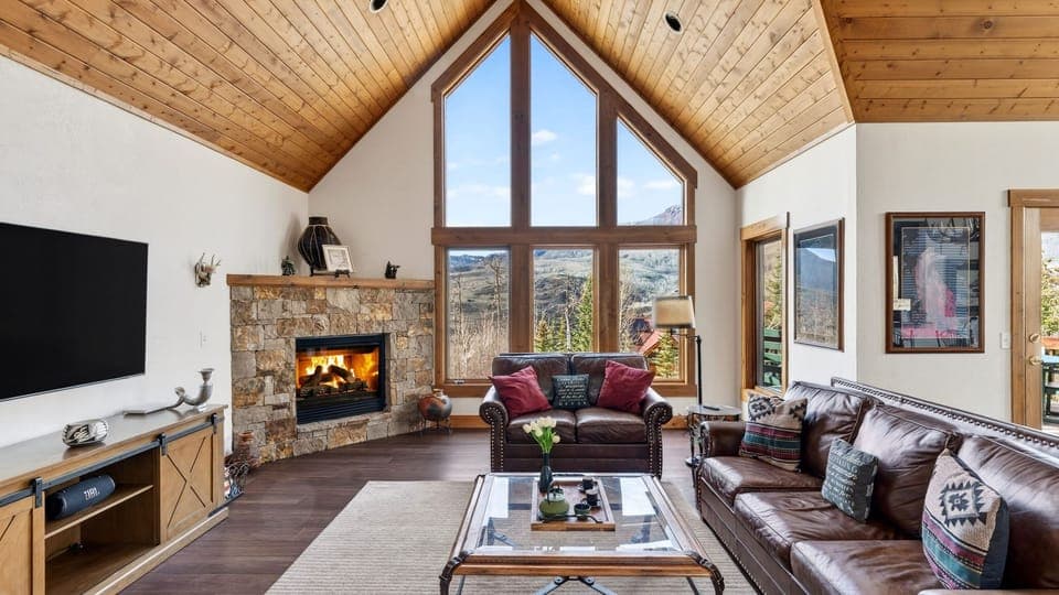 Cozy mountain-inspired living with soaring wood ceilings, a stone fireplace, and stunning floor-to-ceiling views.