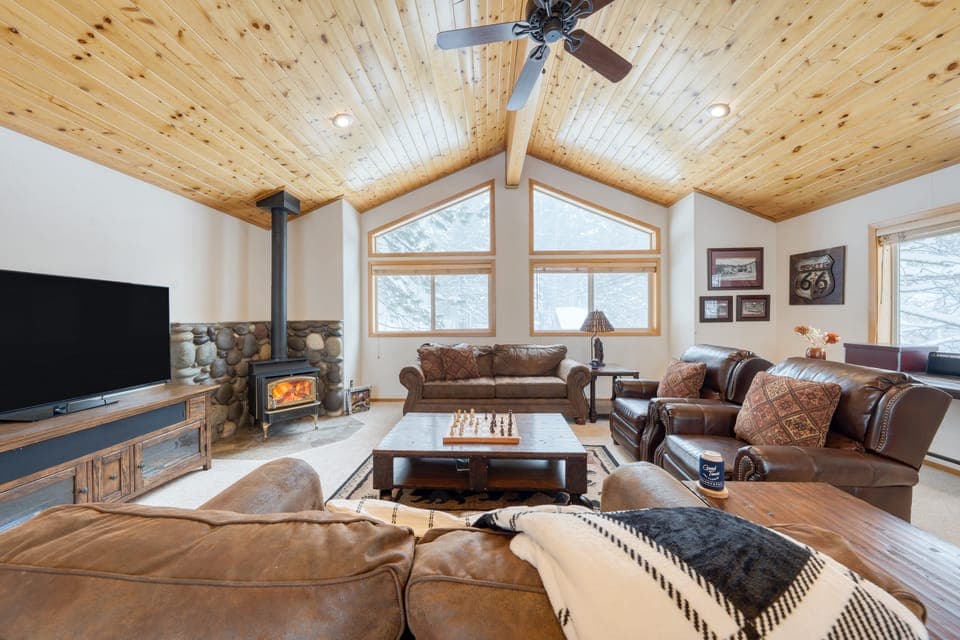A cozy living room with a high wooden ceiling, large windows, and comfortable seating.