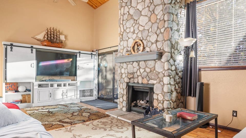 Living area with a stone fireplace, TV and large window for a natural light.
