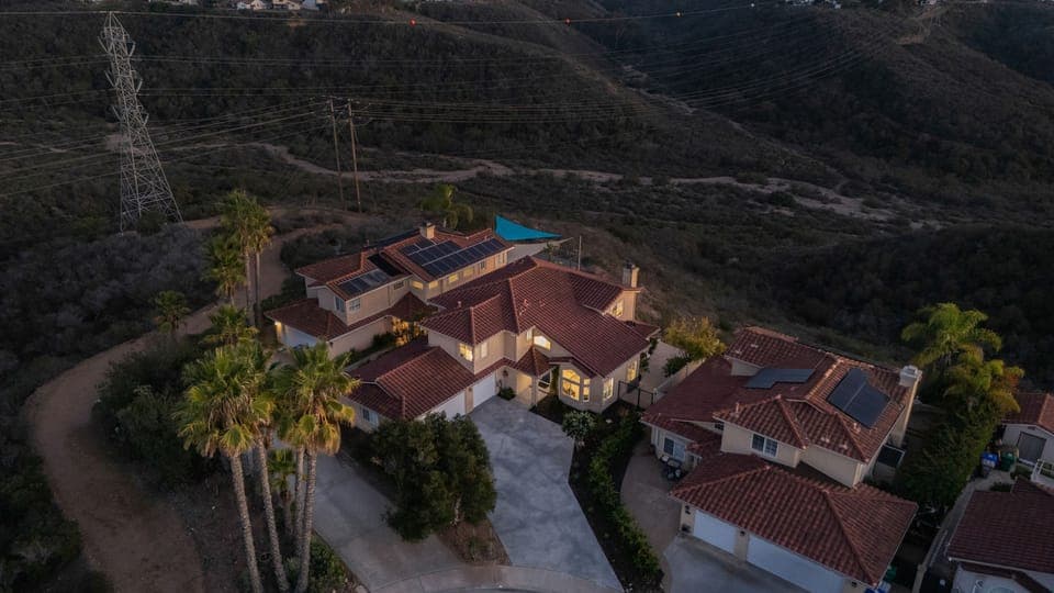 Aerial view of the large Mediterranean-style home and surrounding hilly landscape at sunset/dusk.