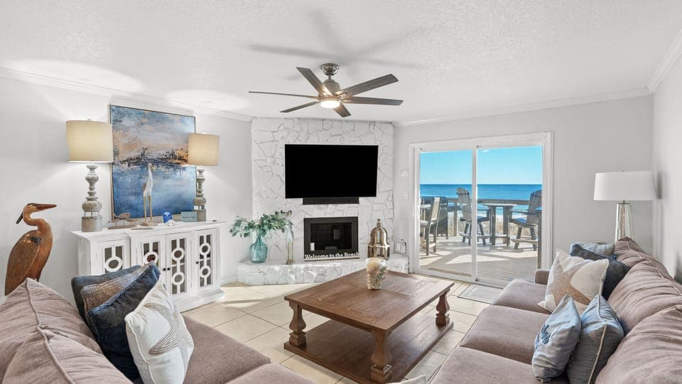 Sun-drenched living room with white stone fireplace and ocean views.