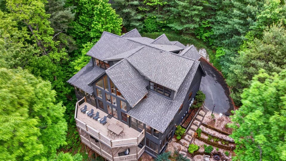 Secluded mountain retreat with expansive wraparound deck, surrounded by lush forest and scenic views.