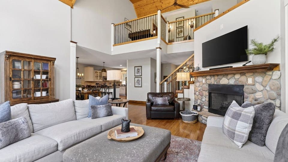 Spacious open-concept living area with soaring ceilings, stone fireplace, and seamless flow into the kitchen and loft.