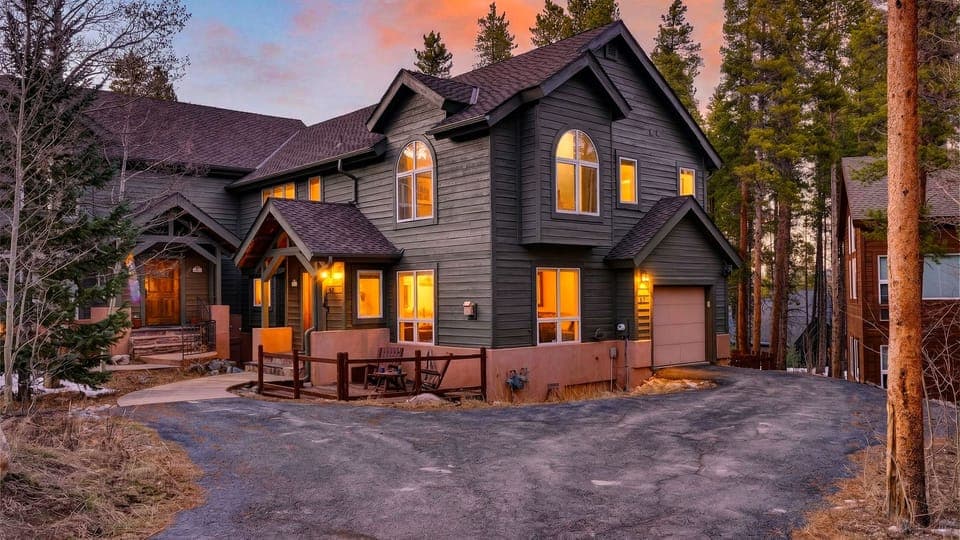 A front-angle view of the dark grey multi-story cabin at dusk with glowing lights.