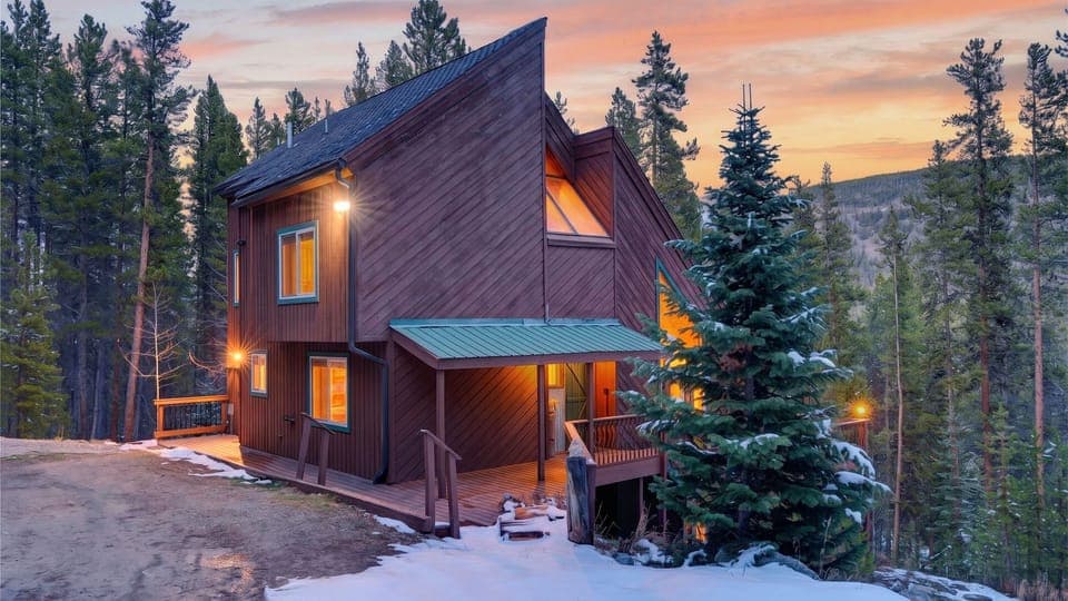 Cozy mountain cabin with warm glowing interiors and scenic forest views at sunset.