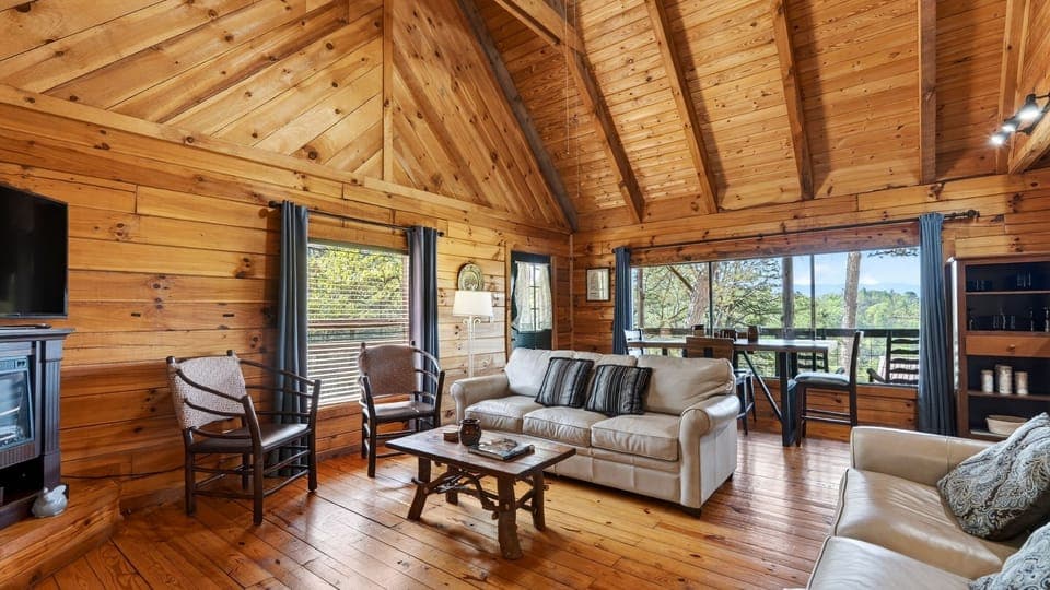 Warm cabin living room with leather sofas, rustic wood accents, and big windows framing peaceful mountain views.