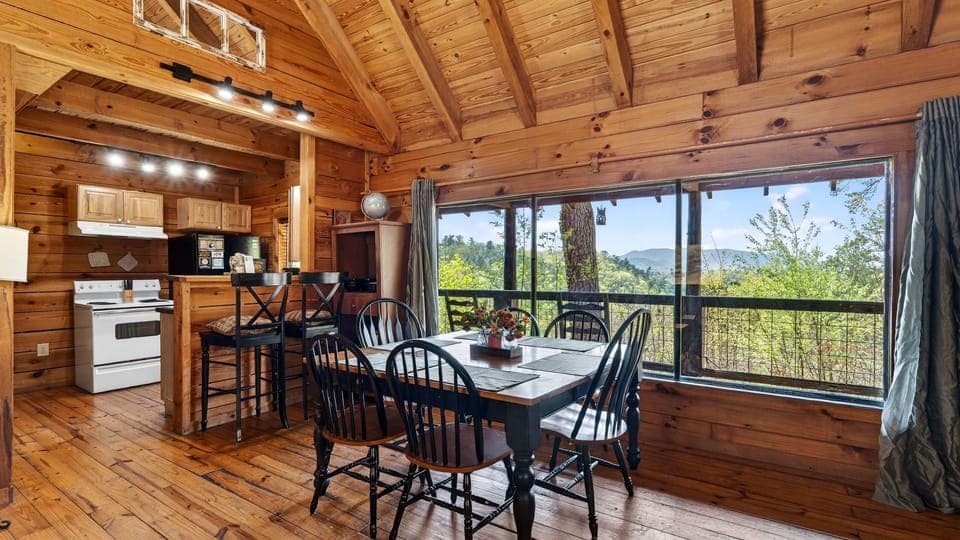 Warm cabin living room with a stone fireplace, queen sleeper sofa, and big windows opening to peaceful mountain views.