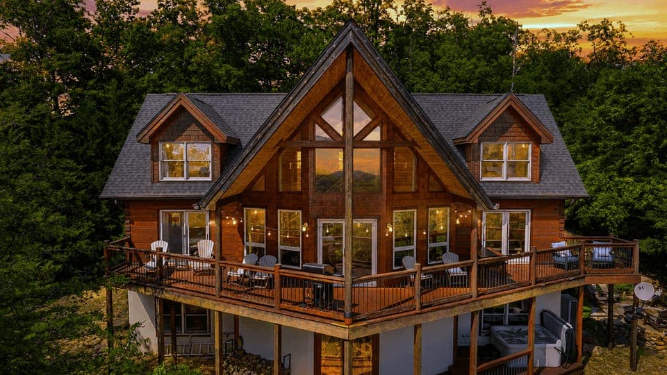 The cabin glows against a dramatic sunset, showcasing the expansive deck.