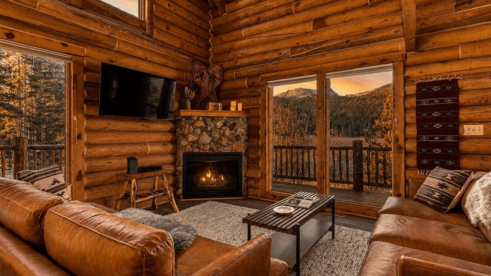 Gather beside the stone fireplace in this soaring log cabin great room with breathtaking mountain views beyond the deck.
