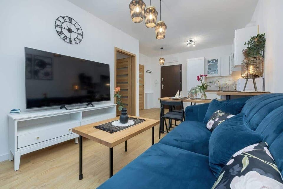 A living room with a blue sectional sofa, coffee table, and wall-mounted TV.
