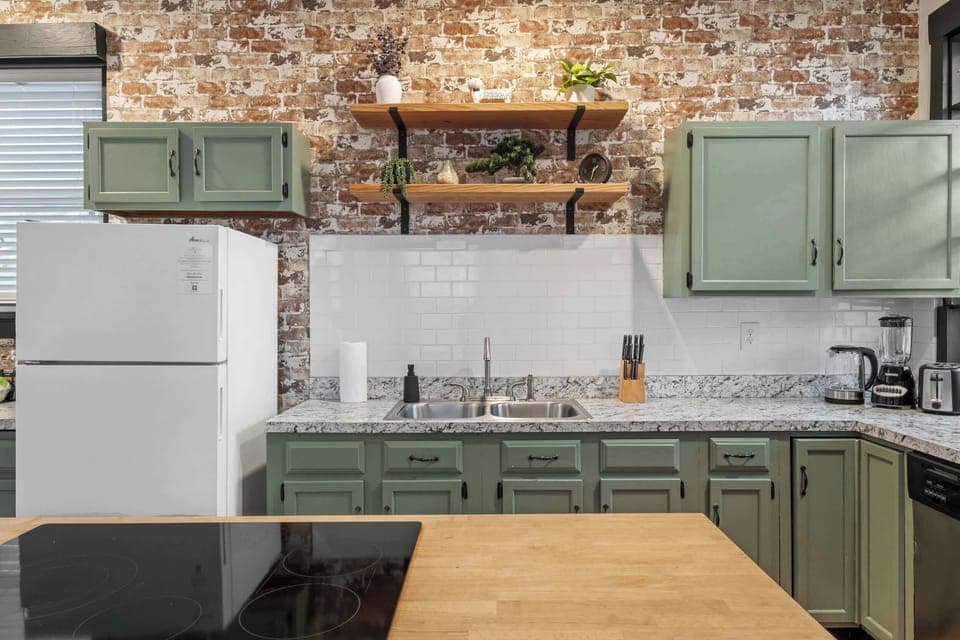 Kitchen: Our kitchen combines modern amenities with rustic charm, featuring a central island for dining and a backdrop of exposed brick.