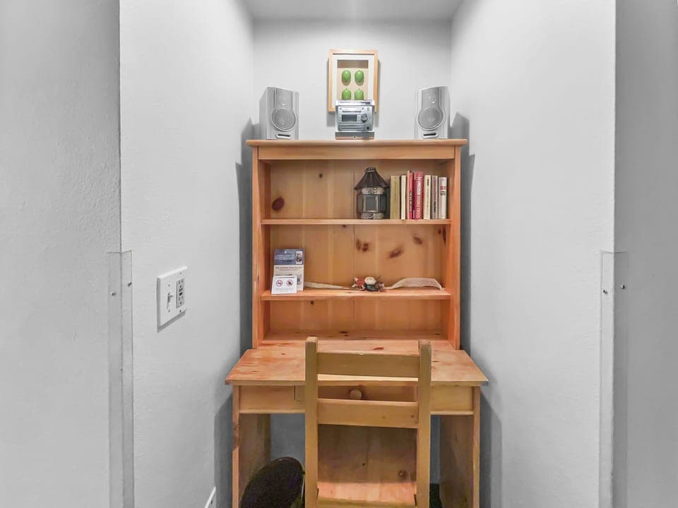 A small wooden desk and chair are set in an alcove, featuring books, a small lamp, and decorative items on the shelves above. A framed picture and speakers are placed on the top shelf.