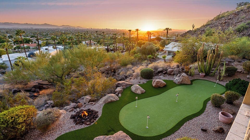 Elegant backyard with a putting green, fire pit, and city views at sunset.