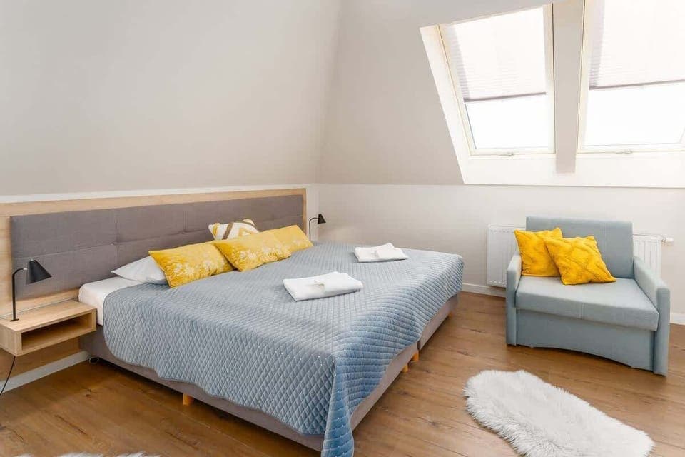 A cozy bedroom with a gray headboard, blue bedspread, yellow cushions, and bright natural light from skylight windows.

