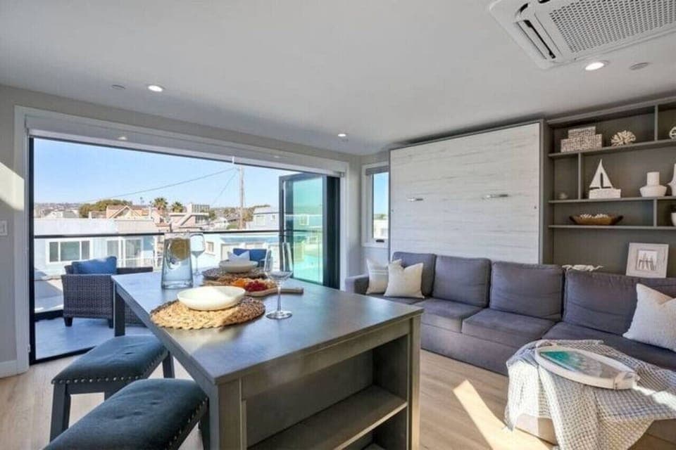 LIVING ROOM – Unwind in the open-concept living room featuring comfortable seating, a flat-screen TV with streaming access, and sliding glass doors that fill the space with natural light and refreshing ocean breezes for a relaxed coastal stay.