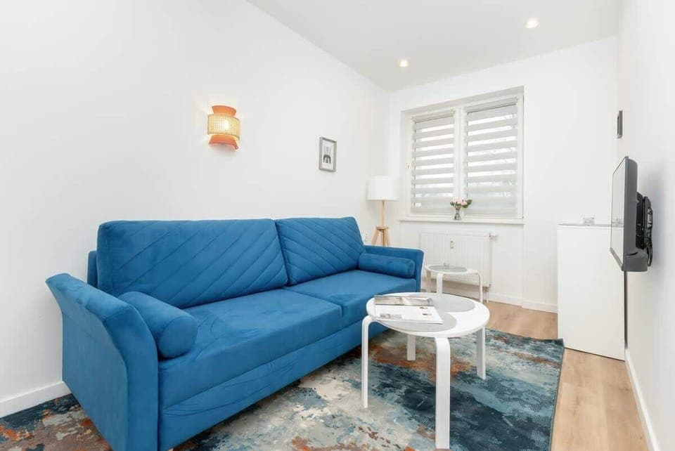 Bright living room with a vibrant blue sofa, white round coffee table, and wall-mounted TV, offering a cozy and modern space for relaxation.
