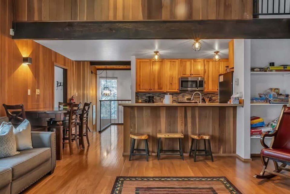 The main living space is a charm-filled area with exposed wood panels and wood beams on the ceilings, stylish decor, and large windows overlooking the trees.