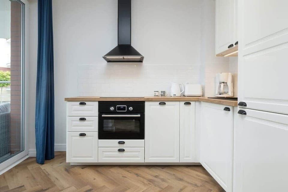 A modern kitchen with white cabinetry, a wooden countertop, and a sleek range hood.


