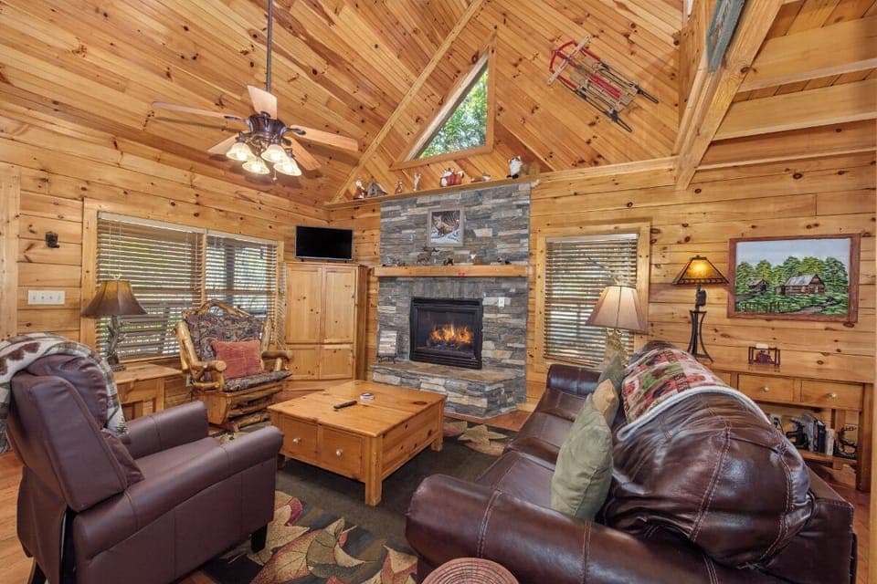 Cozy up by your stone fireplace in this rustic living room with vaulted ceilings and leather seating for mountain getaway relaxation.
