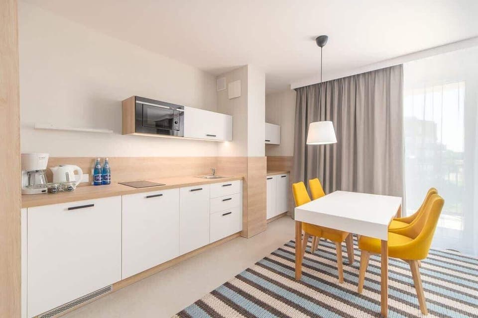 An open-plan kitchen and dining area with white cabinets, wooden countertops, and yellow chairs, blending practicality with a modern design.
