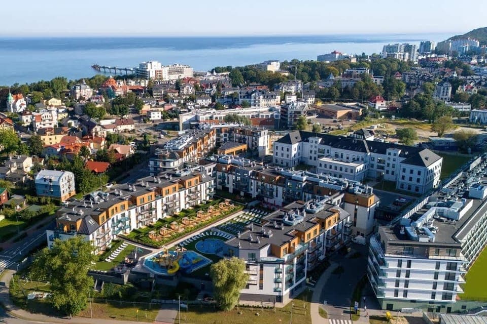 A panoramic aerial view of the neighborhood, highlighting modern architecture, lush greenery, and proximity to the sea.
