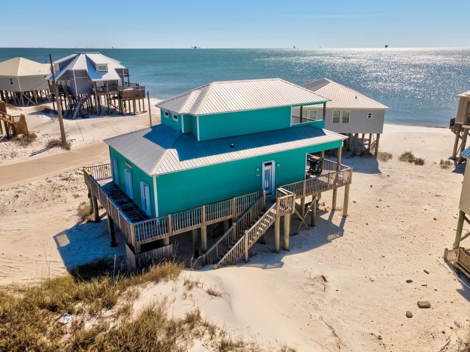 Beachfront vacation home elevated on stilts with direct beach access and stunning Gulf waters backdrop.