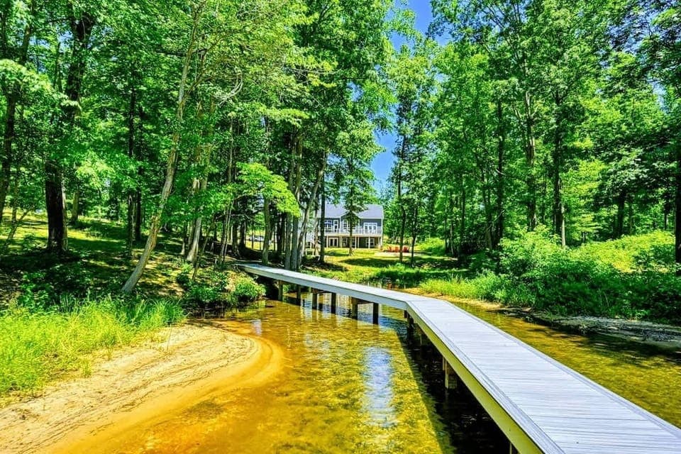 Scenic view of a house nestled in the woods with a private walkway leading to a clear, sandy beach and serene waters