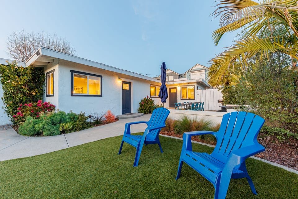 Grassy backyard with blue Adirondack chairs and tropical landsca