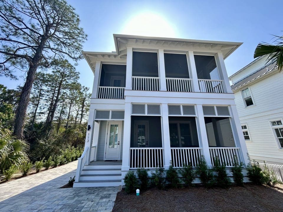 Beautiful two-story coastal home nestled among mature trees, featuring classic white architecture with wraparound porches and modern comfort.
