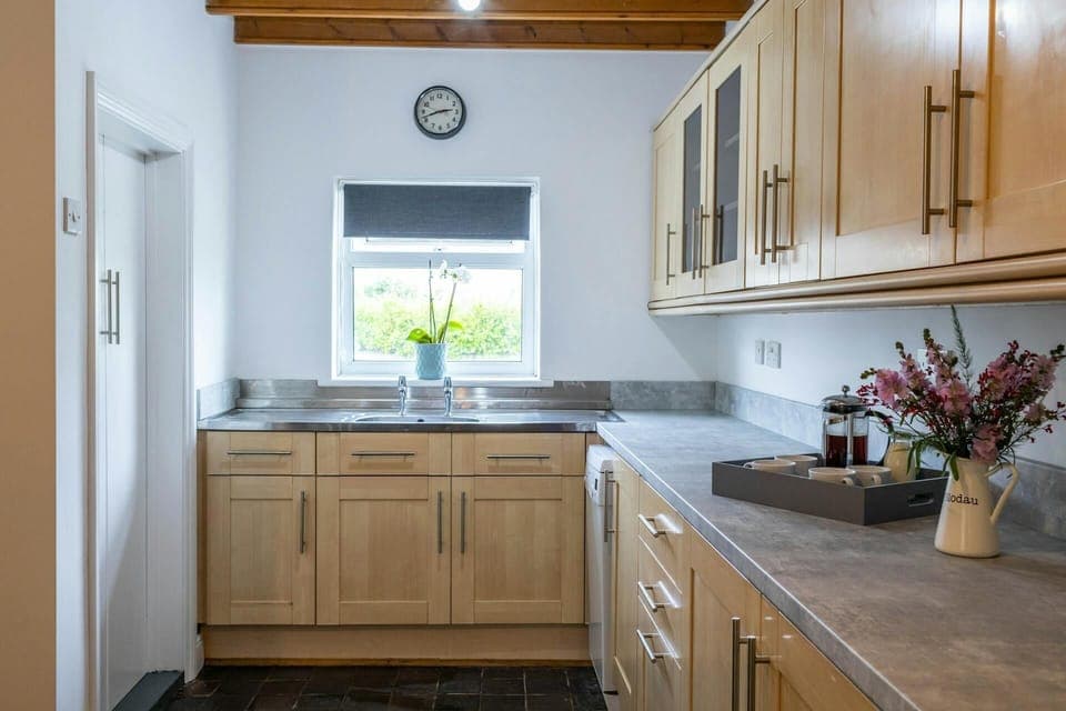 The kitchen with a selection of cupboard, a workspace with a tray of coffee and a bunch of flowers