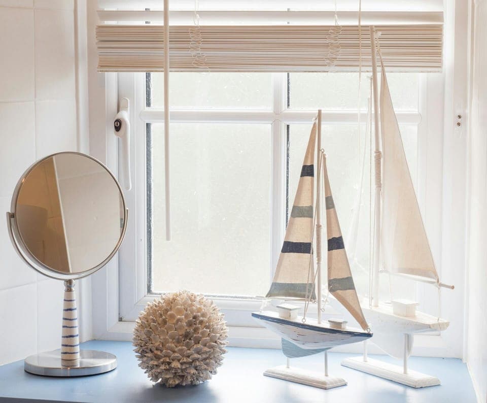 Window sill in bathroom with shaving mirror, sail boat ornaments, blind