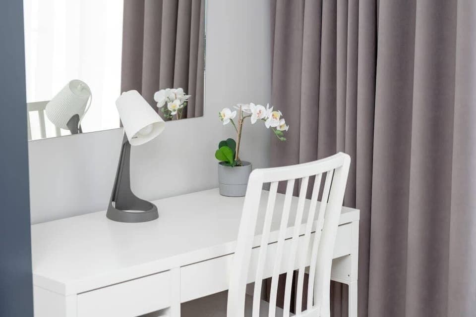 Minimalist bedroom corner with white desk, grey curtains, and modern decor – ideal for working or studying.