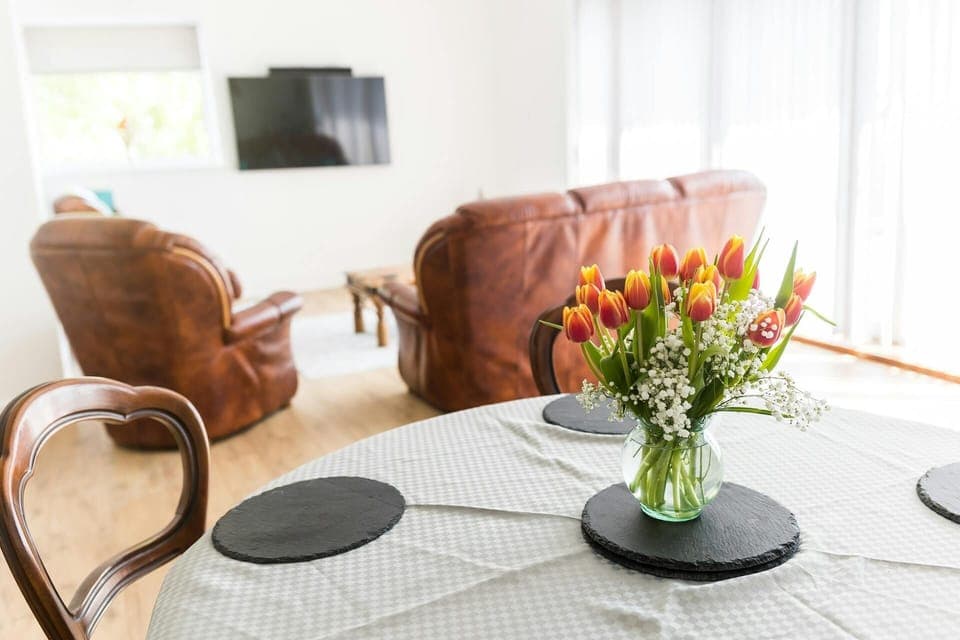 Table set with cloth and flower vase behind living room chairs.