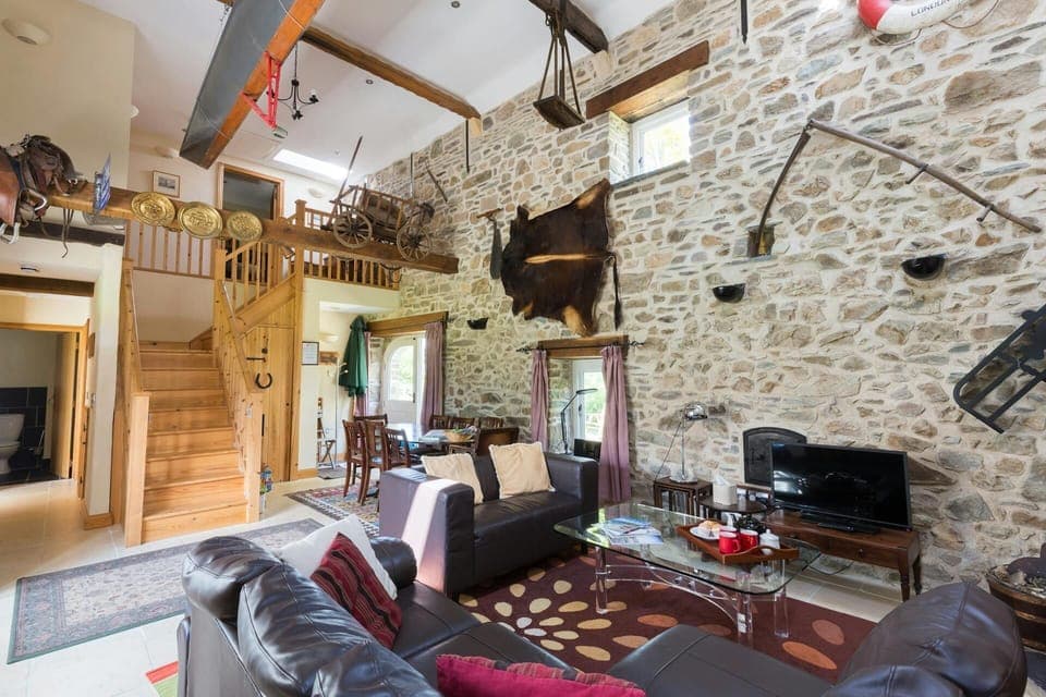 Living area with vaulted ceiling, sofas, glass coffee table, TV, staircase