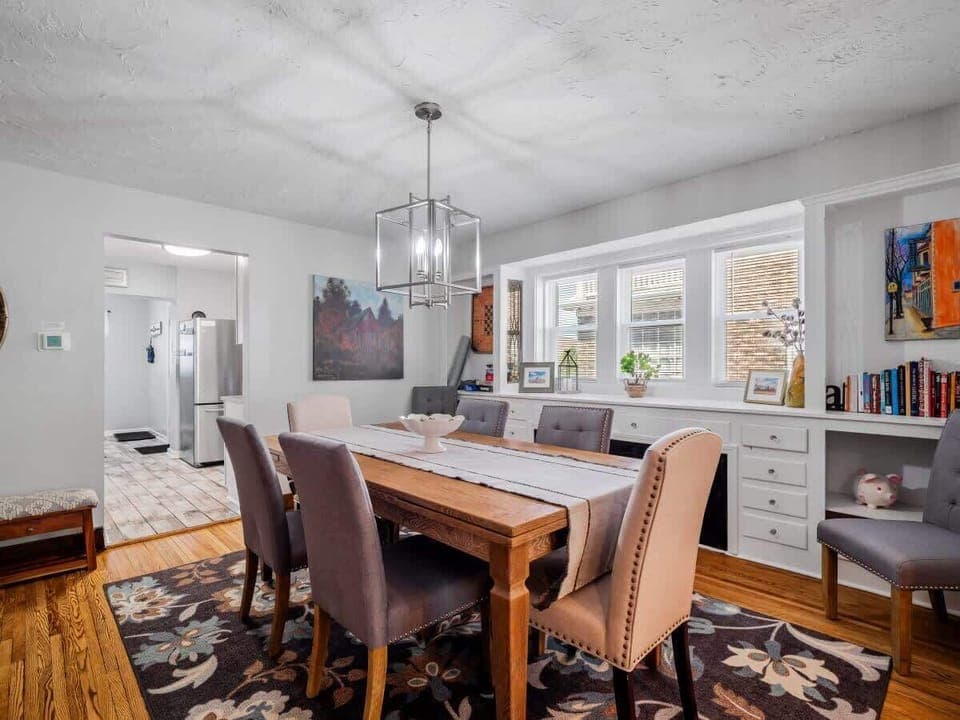 Gather around this spacious dining area featuring a solid wood table for six, elegant chandelier lighting, cozy upholstered chairs, and built-in storage under bay windows—ideal for family meals or game nights! ️