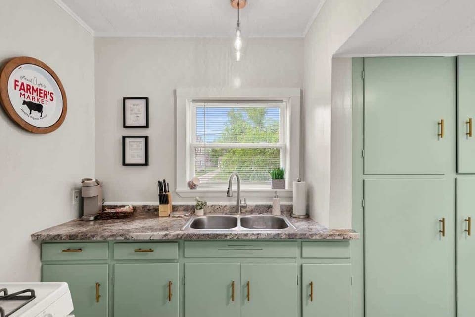 Charming kitchen sink area featuring unique pastel green cabinets, a double sink, and delightful farmhouse decor. 🧑‍🍳🌿