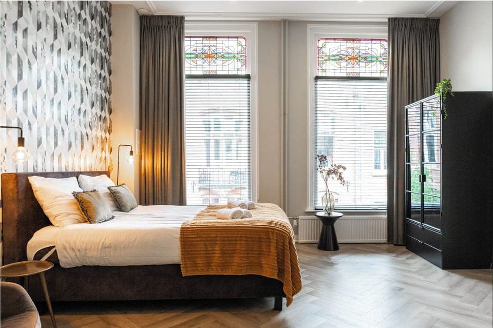 Bright and cozy bedroom featuring large windows with natural light, offering a comfortable and stylish space for a peaceful rest.