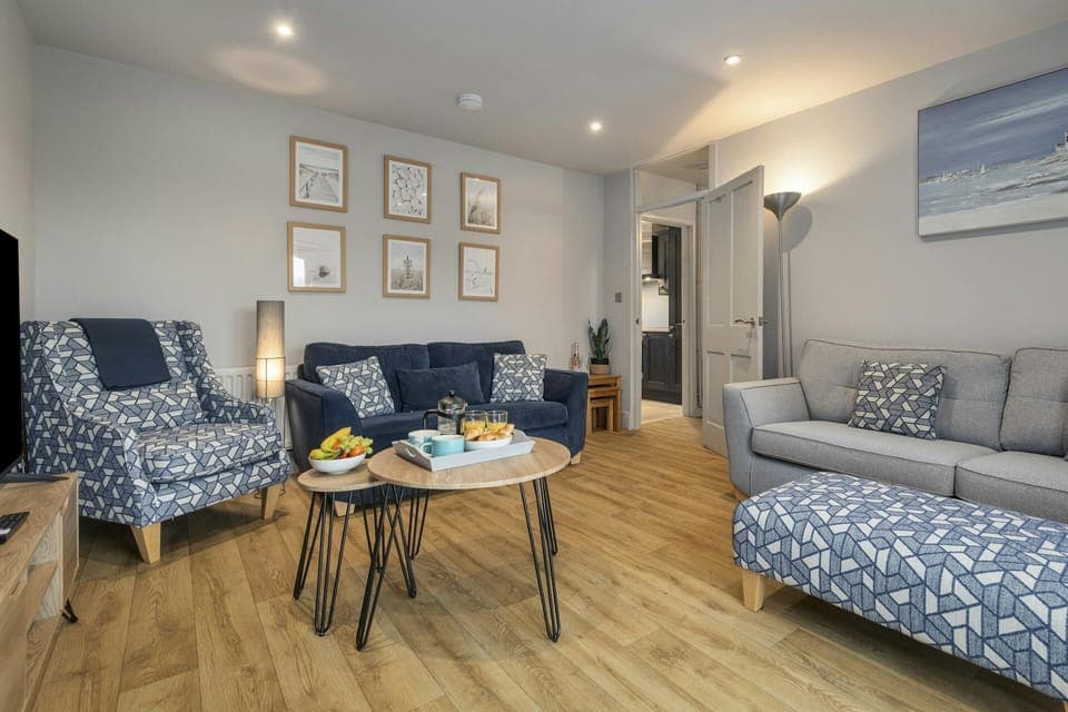 Living room with grey sofa, patterned armchair and footstool, and round coffee table with snacks