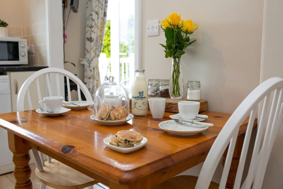 Dining table dressed for dinner for two with welsh cakes and fresh milk, yellow roses in a vase