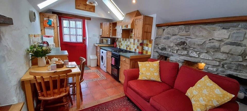 Open plan room in Ty Gwennol with sofas, dining table and chairs, kitchen and door
