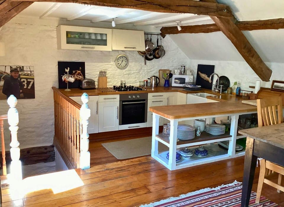 Open kitchen with extended worktop with open storage underneath, microwave, oven, kettle, toaster and gas hob.