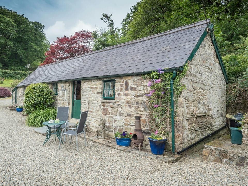 Cottage with gravel patio area with small table and chairs, surrounding trees