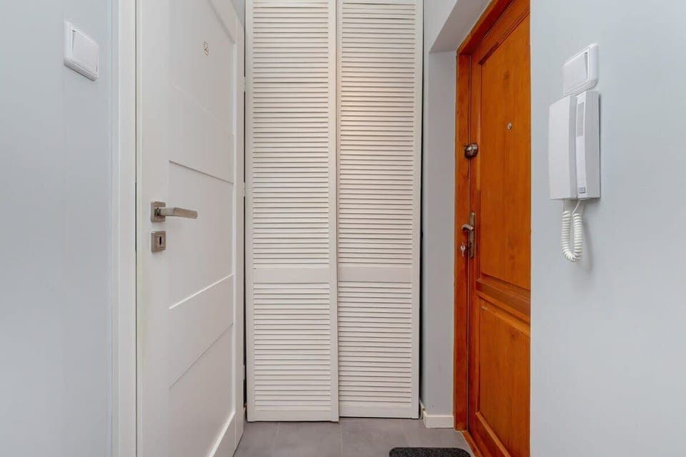 A tidy entryway with a white door, wall hooks, and a wooden bench in a light-toned hallway.

