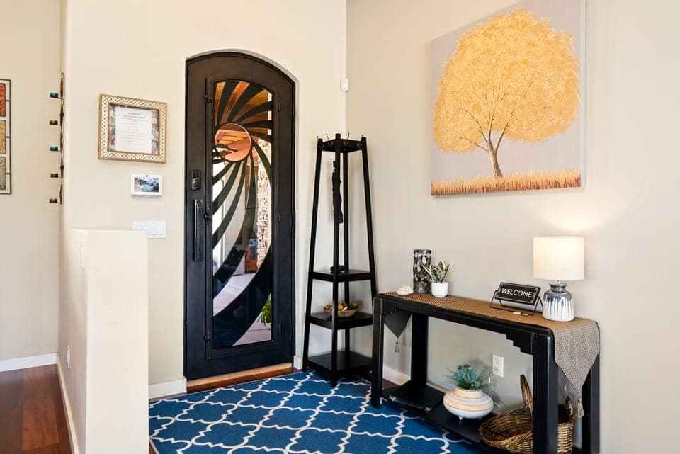 This sophisticated foyer makes a grand statement with a custom sunburst glass door and a vibrant blue patterned rug. The sleek console table and warm tree artwork create a welcoming first impression.