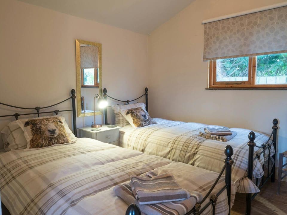 Bedroom with two beds, one bedside drawer unit and lamp, mirror, window