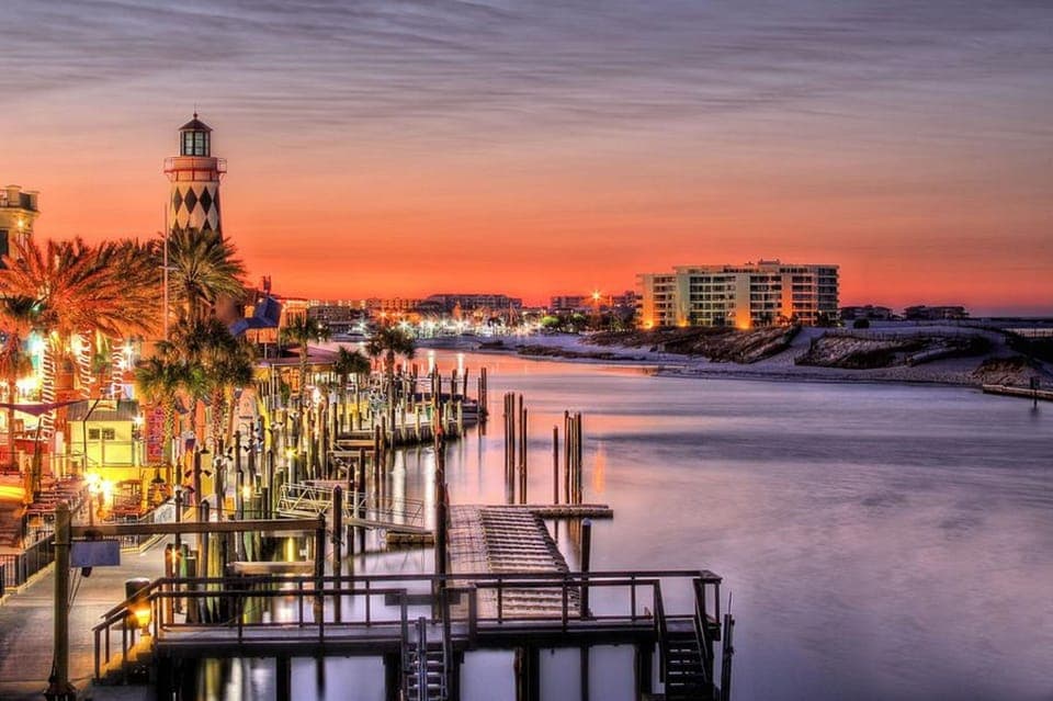 Waterfront area featuring marina docks, lighthouse, and coastal buildings bathed in sunset colors.