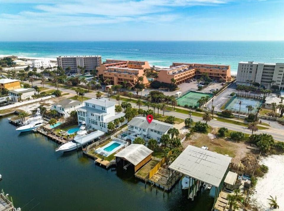 Coastal community aerial view showcasing waterfront properties, tennis courts, and beachfront hotels along pristine shores.