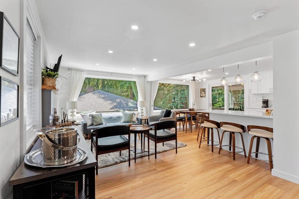 - Open concept living and dining area with style  
- Bright space with forest views through large windows  
- Perfect for gatherings with modern seating and bar stools  
