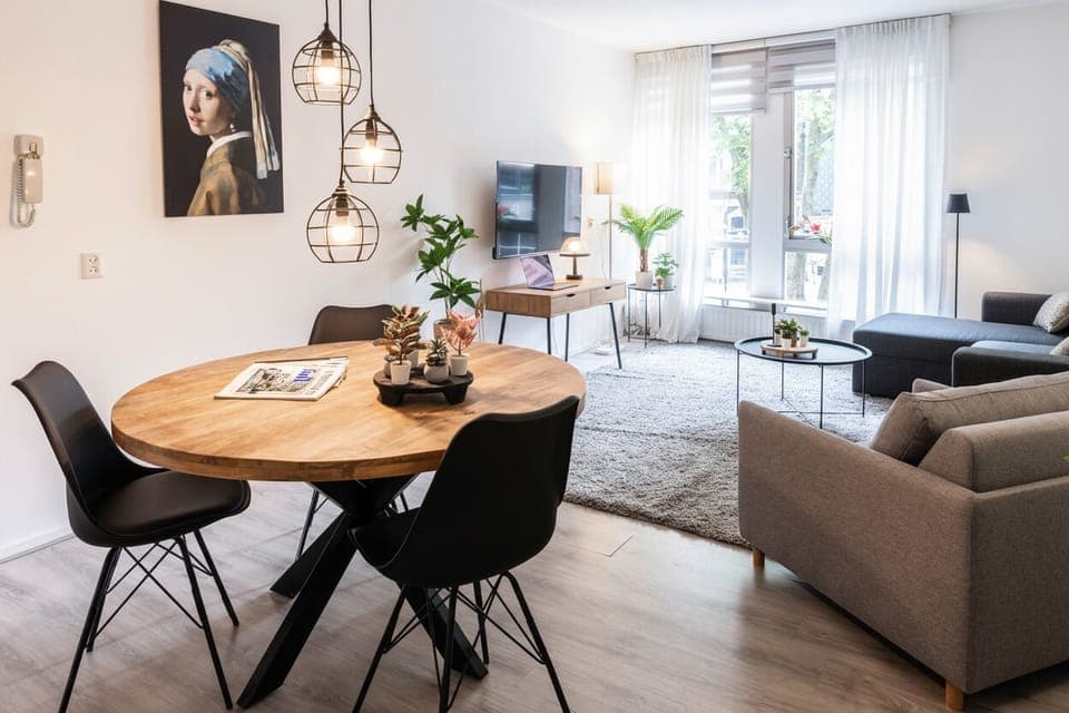 Open-layout living room in Tilburg with a cozy dining area, smart TV, and large windows that fill the space with natural light — perfect for a relaxing stay.