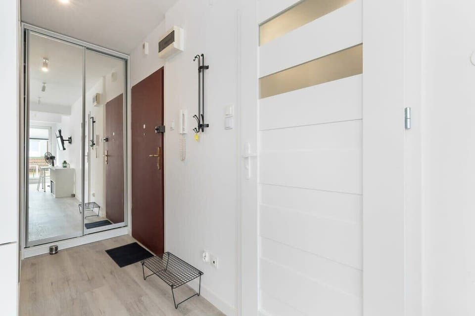 A narrow hallway with a mirror, door, and bright lighting. A small but functional transition space.